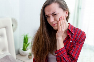 woman in red flannel shirt suffering from jaw pain holds her face