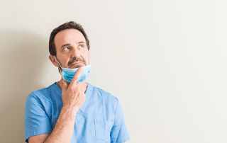 A dentist wearing a mask and holding his finger to his chin in concentration