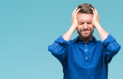 man in blue shirt holding his head suffering from chronic migraine, could be TMD?