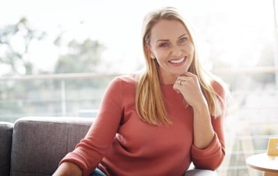 woman in red shirt sitting on couch smiling with teeth